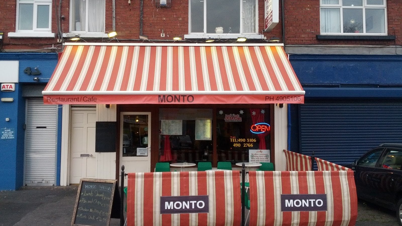 The red-and-cream striped awning and pavement tables outside Montos on Sundrive Road, Kimmage, lit up at dusk